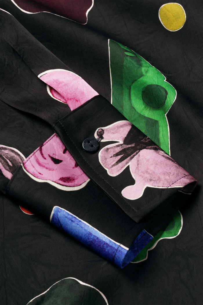 Black garment with pink green blue and yellow abstract shapes folded on a dark surface