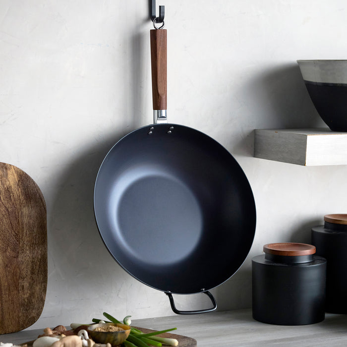 Black wok with wooden handle hanging from a pot rack