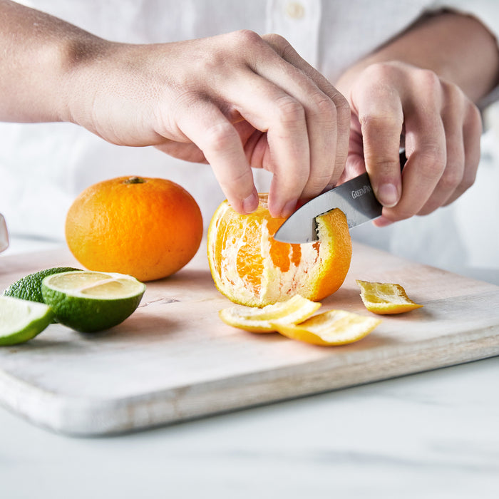 Hand holding a walnut-handled knife peeling an orange.
