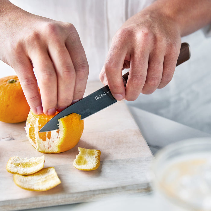 Premiere Titanium knife peeling an orange on a cutting board with slices and orange peel nearby.