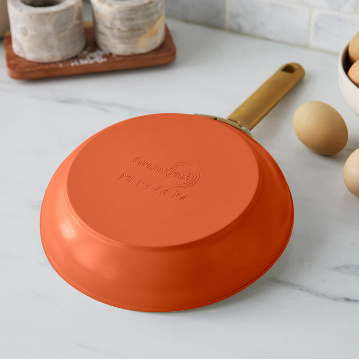 Dark orange frying pan with a gold handle on a marble countertop