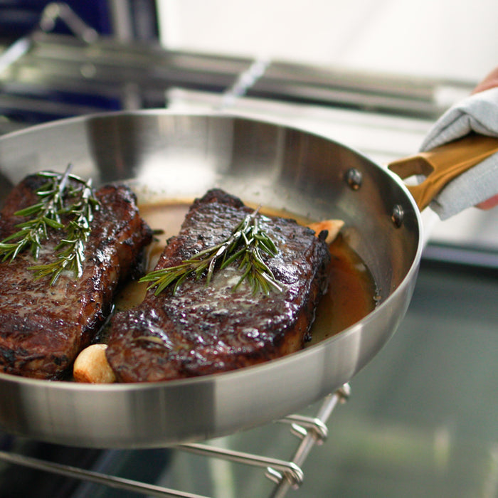 Two steaks with rosemary in a stainless steel pan on an oven rack