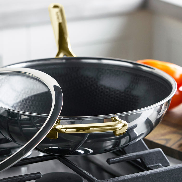 Gold hybrid ceramic nonstick wok with lid on a stove next to a tomato.