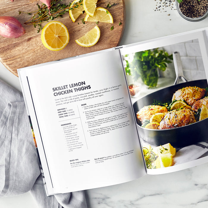 Cookbook open to a lemon chicken thighs recipe, with cooked chicken and lemon slices on the counter.