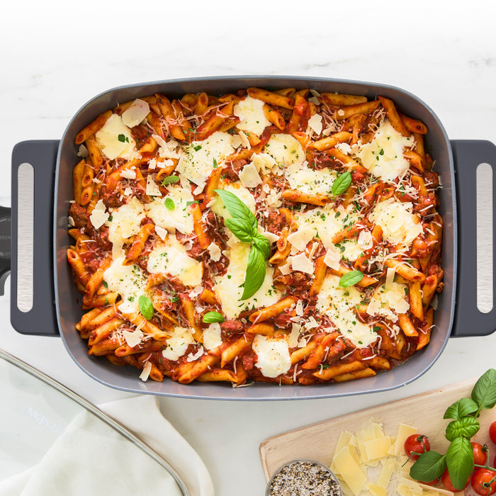 Penne pasta baked with tomato sauce, cheese, and basil in a graphite-colored 7-quart skillet.