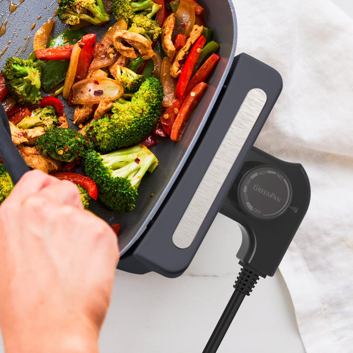 Broccoli and peppers being stirred in a graphite 7-quart skillet on an electric stovetop.
