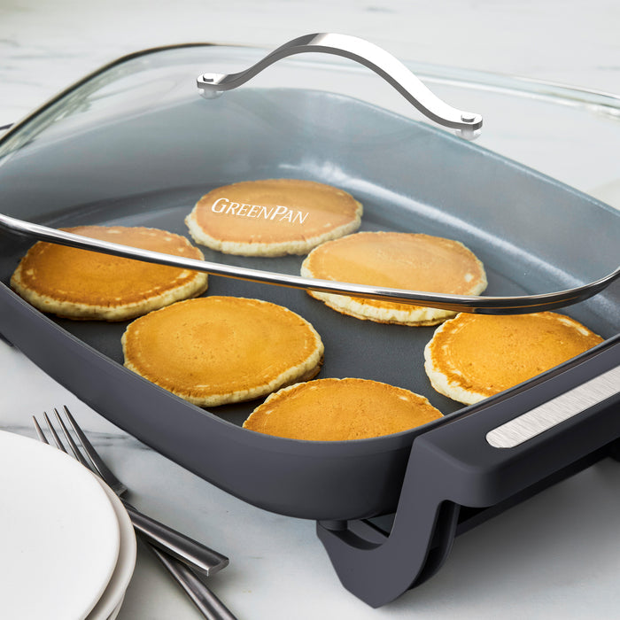 Six pancakes cooking in a graphite 7-quart skillet on a marble countertop.