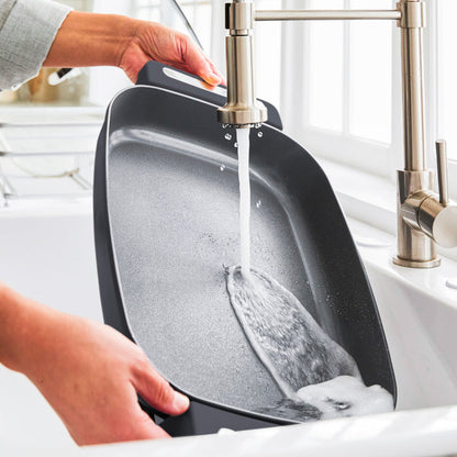 Person washing a graphite 7-quart skillet in a kitchen sink by a window after cooking.
