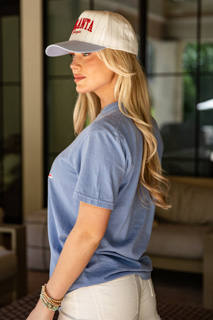 Woman wearing a blue shirt and white cap with 'Atlanta' text, standing indoors.