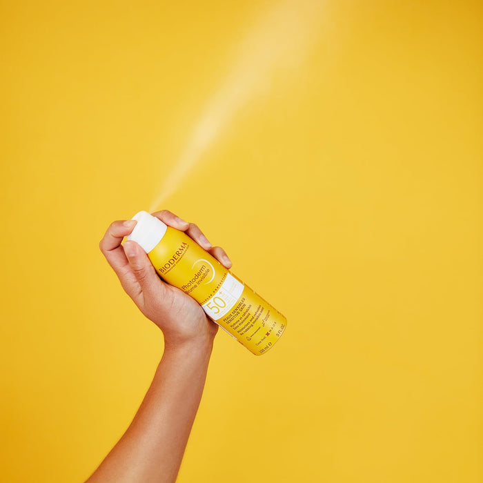 Bioderma Photoderm Invisible Mist SPF50+ 150ml hand spraying into air with yellow background