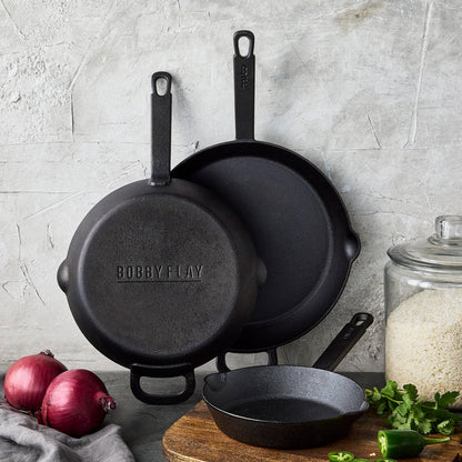 The Bobby Flay by GreenPan 8", 10", and 12" Cast Iron Frypan Set is displayed on a kitchen counter with red onions, cilantro, rice, and sliced jalapeño—ideal for daily use with a spacious cooking surface.