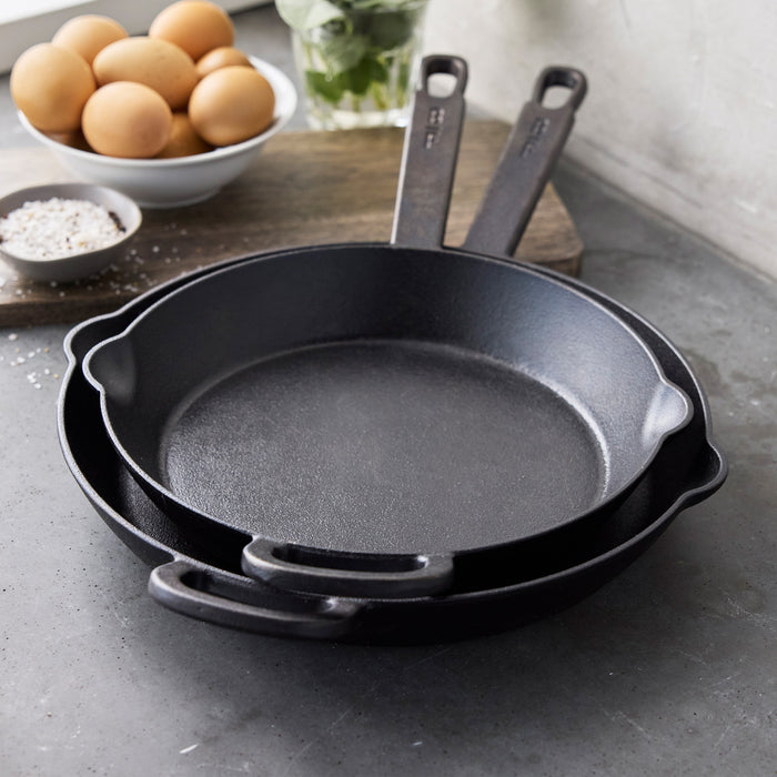 The Bobby Flay by GreenPan 8", 10", and 12" Cast Iron Frypan Set, shown nested on a gray countertop with a bowl of eggs, salt dish, and jar of herbs nearby, features spacious heirloom-quality black skillets.