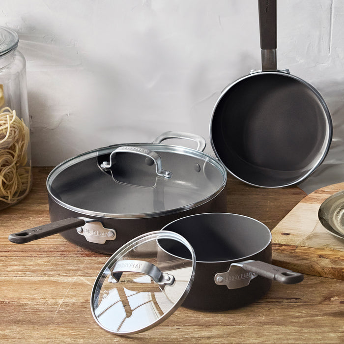 Set of three black ceramic nonstick pots and pans on a wooden surface.