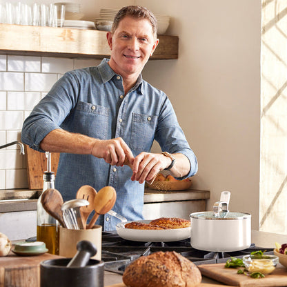 Man in a denim shirt cooks with Bobby Flay by GreenPan ceramic cookware set on a kitchen stove.