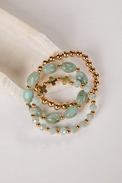 three bracelets with green beads and gold accents on a light gray background