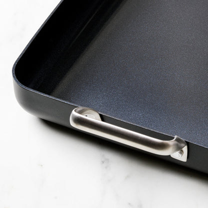 Black aluminum 13.8″ x 10″ rectangular ceramic nonstick roasting pan with metallic side handles on a marble surface.