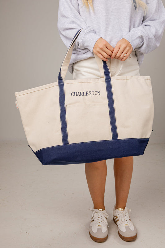 Person holding a white tote bag with blue accents and 'Charleston' printed on it.