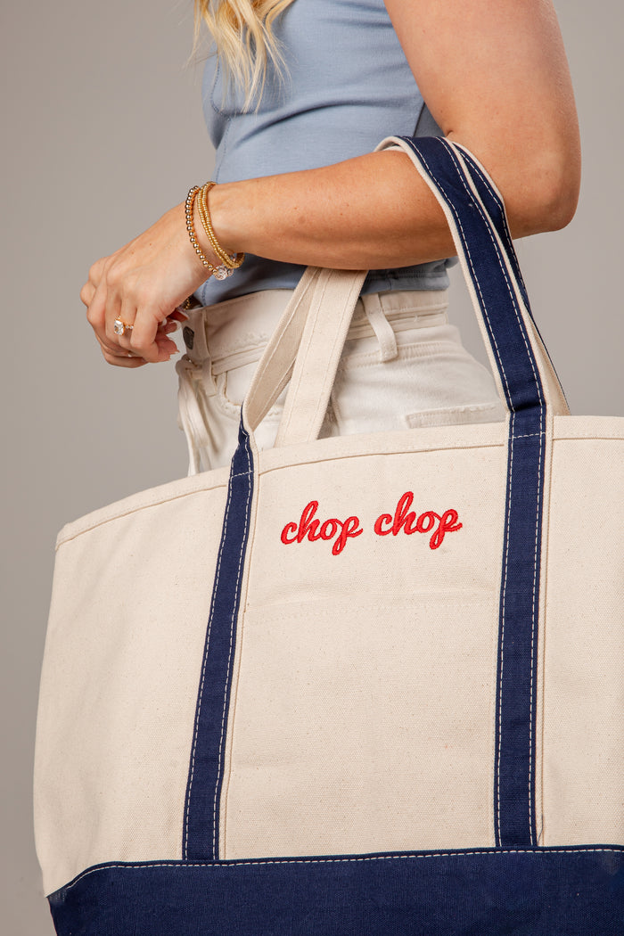 Person holding a tote bag with 'chop chop' text, wearing a blue top and beige pants.