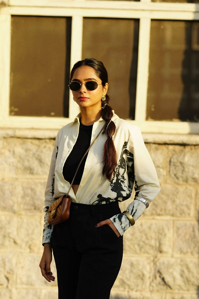 Woman wearing the white and grey CM shirt with black trousers and sunglasses, outdoors, front view