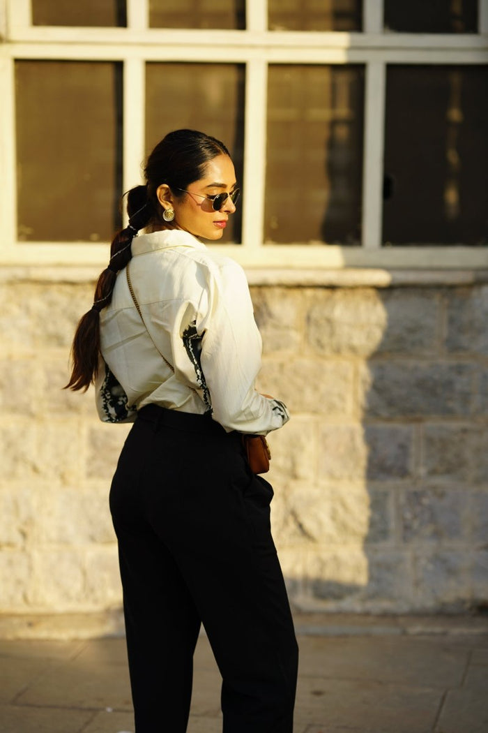 Woman wearing the CM shirt with black trousers, outdoors, back three-quarter view, looking over her shoulder