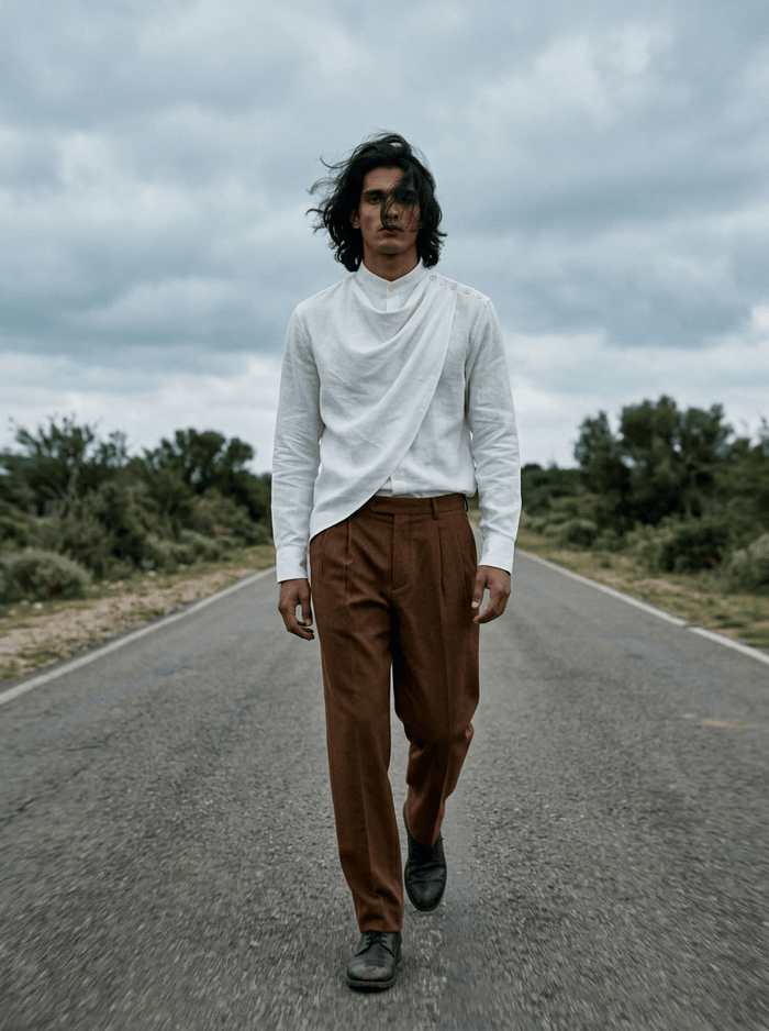 Man wearing the white Cowl shirt with brown trousers, full length front view, walking on an open road