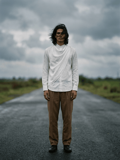 Man wearing the white Cowl shirt with brown trousers, full length front view, standing on a road under cloudy sky