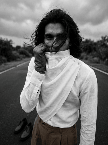 Black and white photo of a man wearing the Cowl shirt, hand at the cowl neckline, on a road