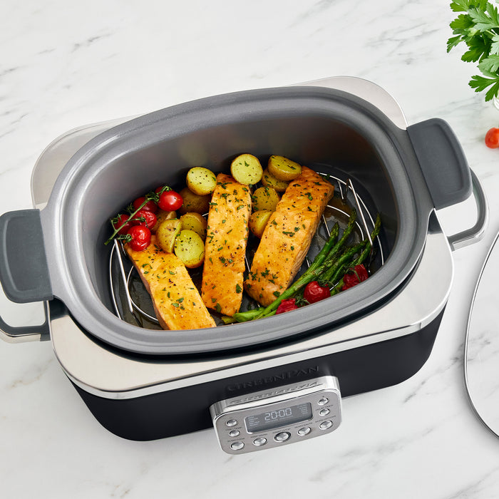 Black slow cooker with salmon and vegetables on a marble surface