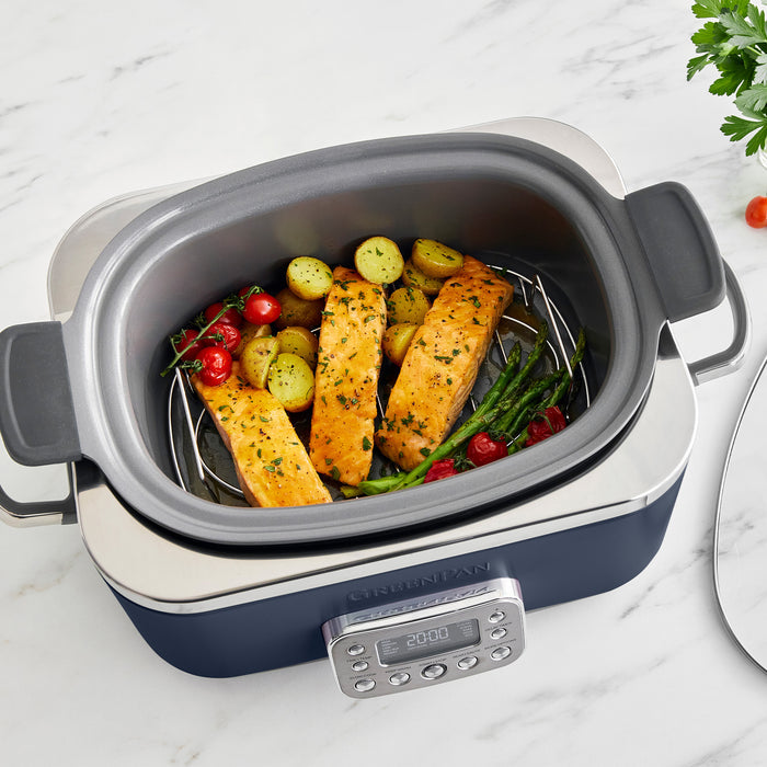 Blue slow cooker with salmon and vegetables on a marble surface