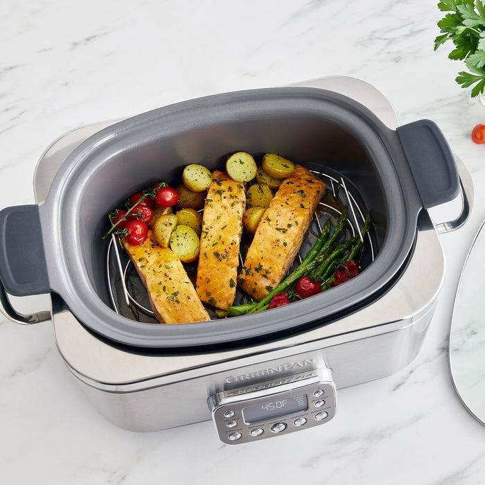 Stainless steel slow cooker with salmon and vegetables on a marble surface