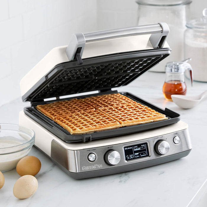 Ceramic 4-square waffle maker in cream with Liège waffles, eggs, batter, and syrup on the counter.