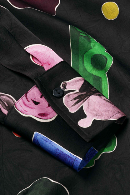 Black garment with pink green blue and yellow abstract shapes folded on a dark surface