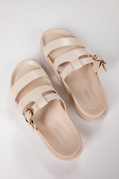 Pair of beige sandals with gold buckles on a light gray background