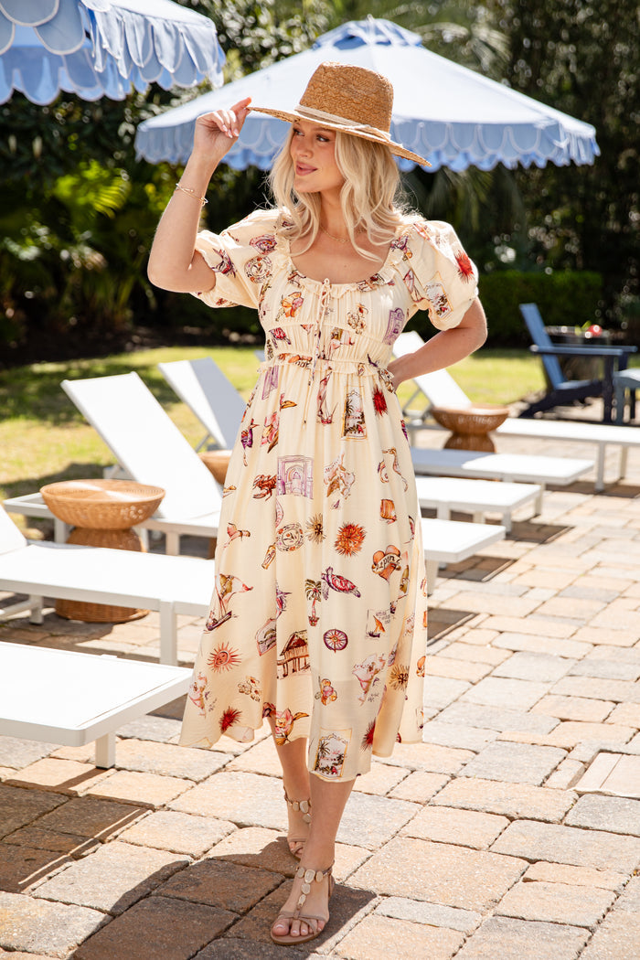 Woman in a floral dress standing outdoors with lounge chairs and umbrellas in the background
