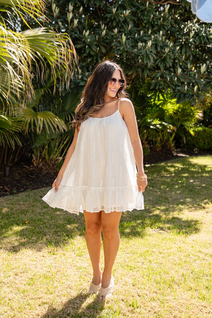 Woman in a white dress standing outdoors with greenery in the background