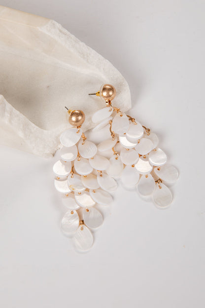 Pearl and gold earrings hanging from a white shell on a light gray background