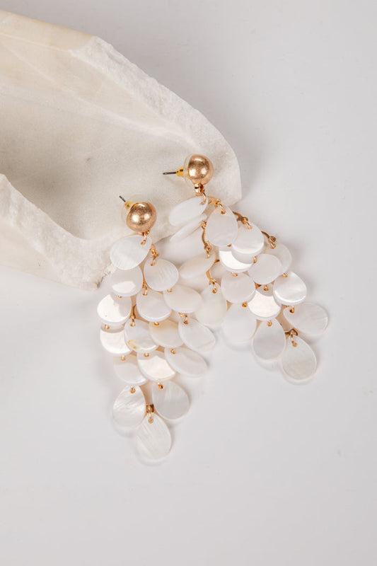 Pearl and gold earrings hanging from a white shell on a light gray background