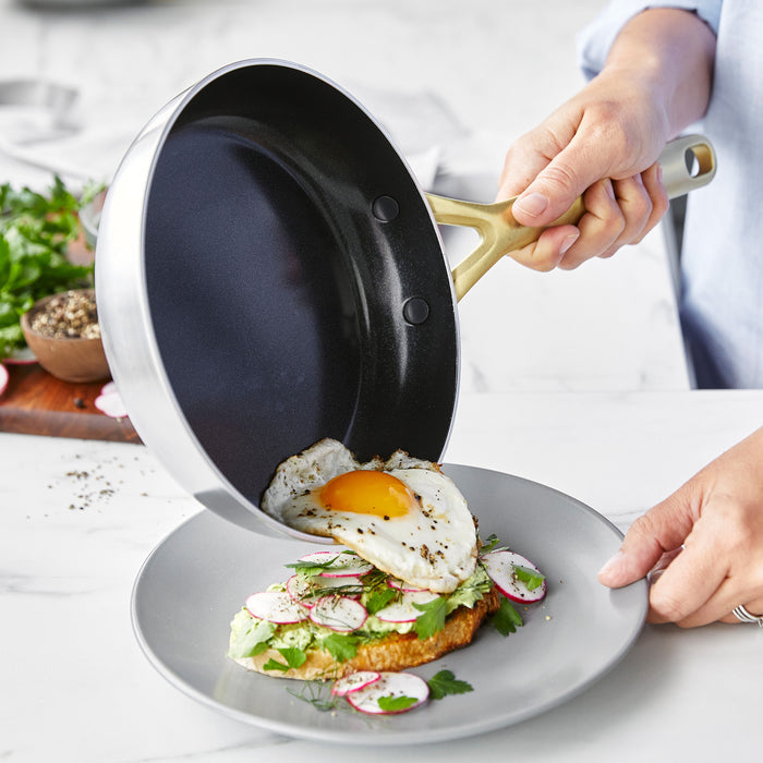Sunny-side-up egg being slid from a stainless steel frypan onto avocado toast with radishes on a plate.