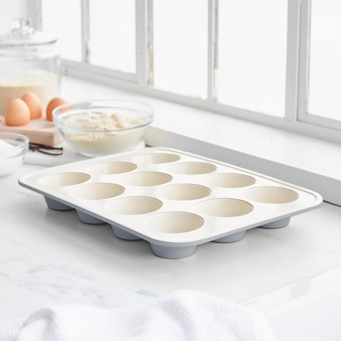 Gray ceramic nonstick muffin pan on a kitchen counter with baking ingredients nearby.