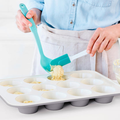 Muffin batter being spooned into a gray ceramic nonstick muffin pan using a teal spatula.