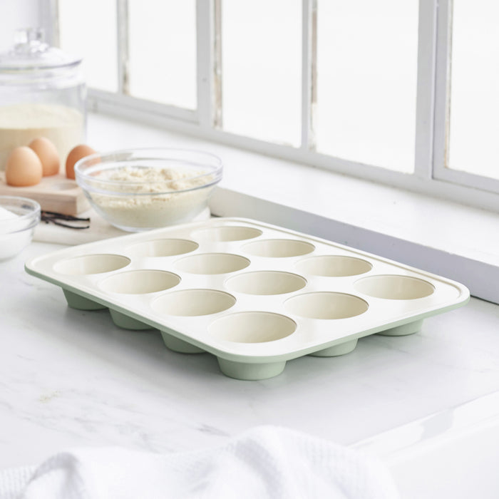 Sage green ceramic muffin pan with nonstick surface on a countertop.