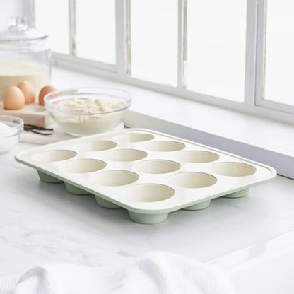 Sage green ceramic muffin pan with nonstick surface on a countertop.