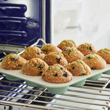 Blueberry muffins in a sage green ceramic nonstick muffin pan, 12-cup capacity, on a countertop.