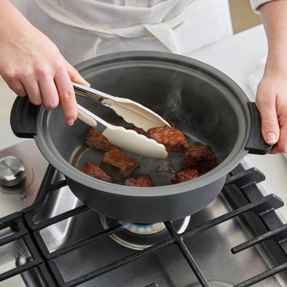 Person using tongs to handle food in a pot on a stove