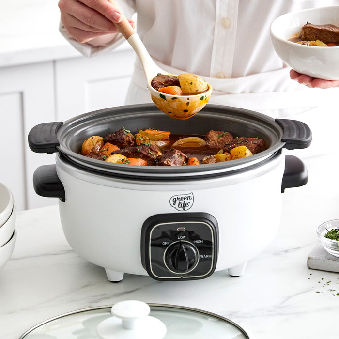 White slow cooker with beef stew, person serving with a ladle, on a countertop