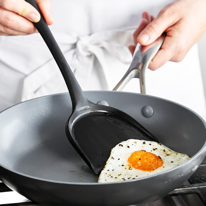 Hand lifting a fried egg from a skillet with a GreenPan spatula on the stove.