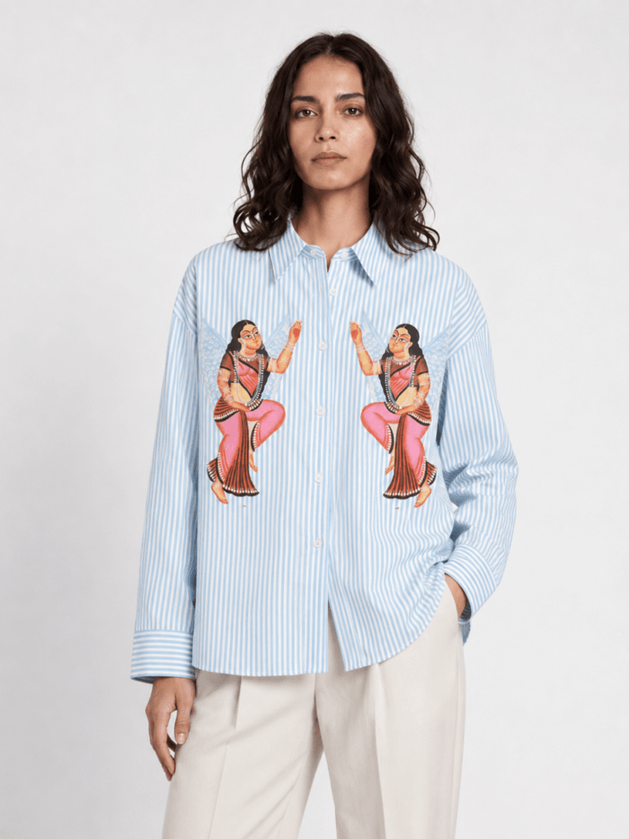 Woman wearing the blue striped Kalighat Graffiti shirt with cream trousers, front view, hand in pocket