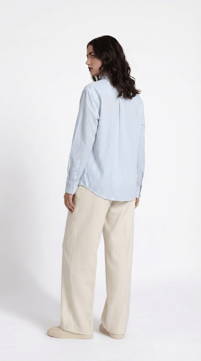 Woman wearing the blue striped Kalighat Graffiti shirt with cream trousers, back view, looking over her shoulder