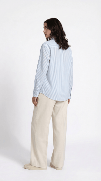 Woman wearing the blue striped Kalighat Graffiti shirt with cream trousers, back view, looking over her shoulder