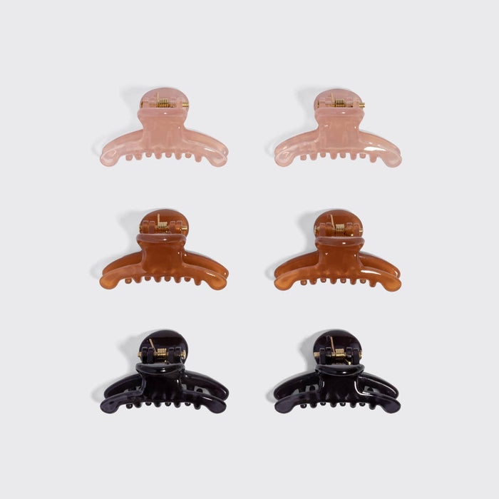 Six hair claw clips arranged in two columns of three on a light gray background. The clips come in translucent pale pink, warm amber-brown, and glossy black finishes, each with a small gold metal accent on the inner band.